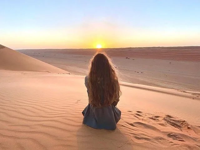 Una mujer sentada en una duna de arena, contemplando el atardecer en el desierto.