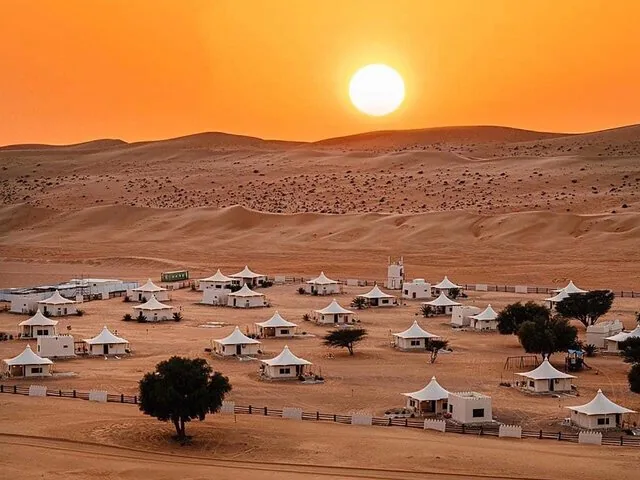 Des tentes blanches dans un campement du désert sous un grand soleil couchant dans le désert de Wahiba.