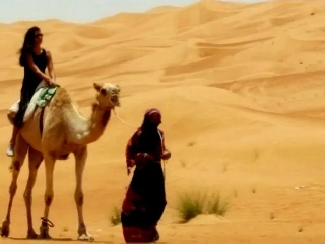 A woman riding a camel led by a local guide in the desert.