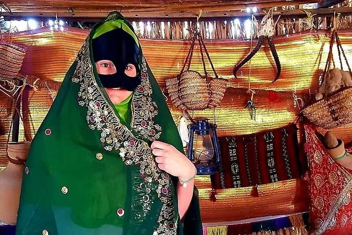 A person wearing a traditional face mask and green headscarf in a decorated tent.