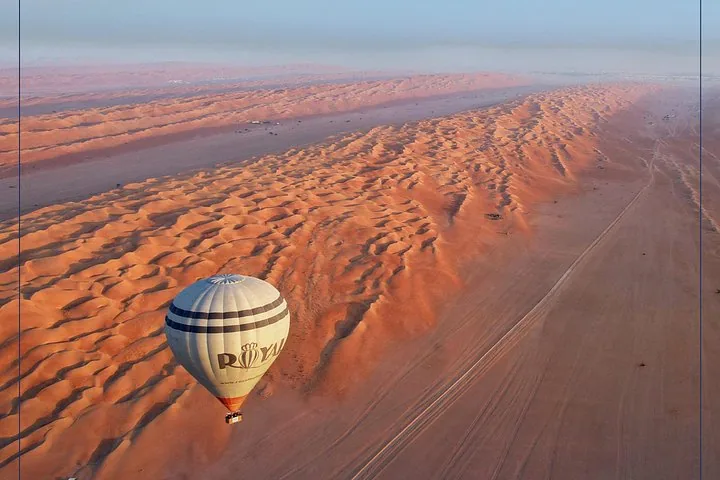 A hot air balloon flying over the rippling sand dunes of the desert.